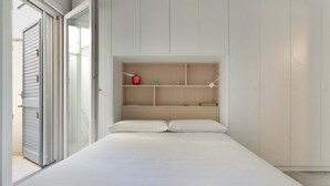 A bedroom with a bed, a built-in shelf unit, and a sliding glass door leading to a balcony. - 1991 Suite Verdi (Lecce)