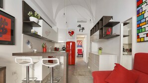 A modern kitchen with white bar stools, a red refrigerator, and a red sofa. - 1991 Suite Verdi (Lecce)