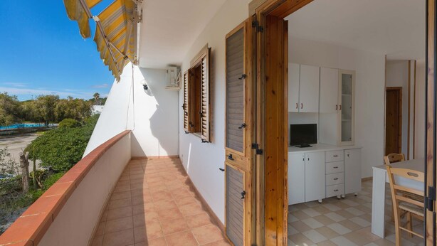 A balcony with a view of the sea, a kitchen area with cabinets and a TV, and a dining area with a chair. - 1892 Casa Di Ronzino (Melendugno)