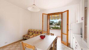 A compact living space with a dining table, chairs, a sofa, and a large window offering a view of greenery. - 1892 Casa Di Ronzino (Melendugno)