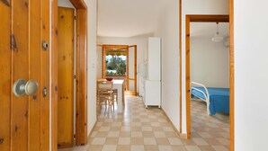 A hallway with a checkered floor, wooden doors, a dining area with a table and chairs, a bed with a blue bedspread, and a white refrigerator. - 1892 Casa Di Ronzino (Melendugno)