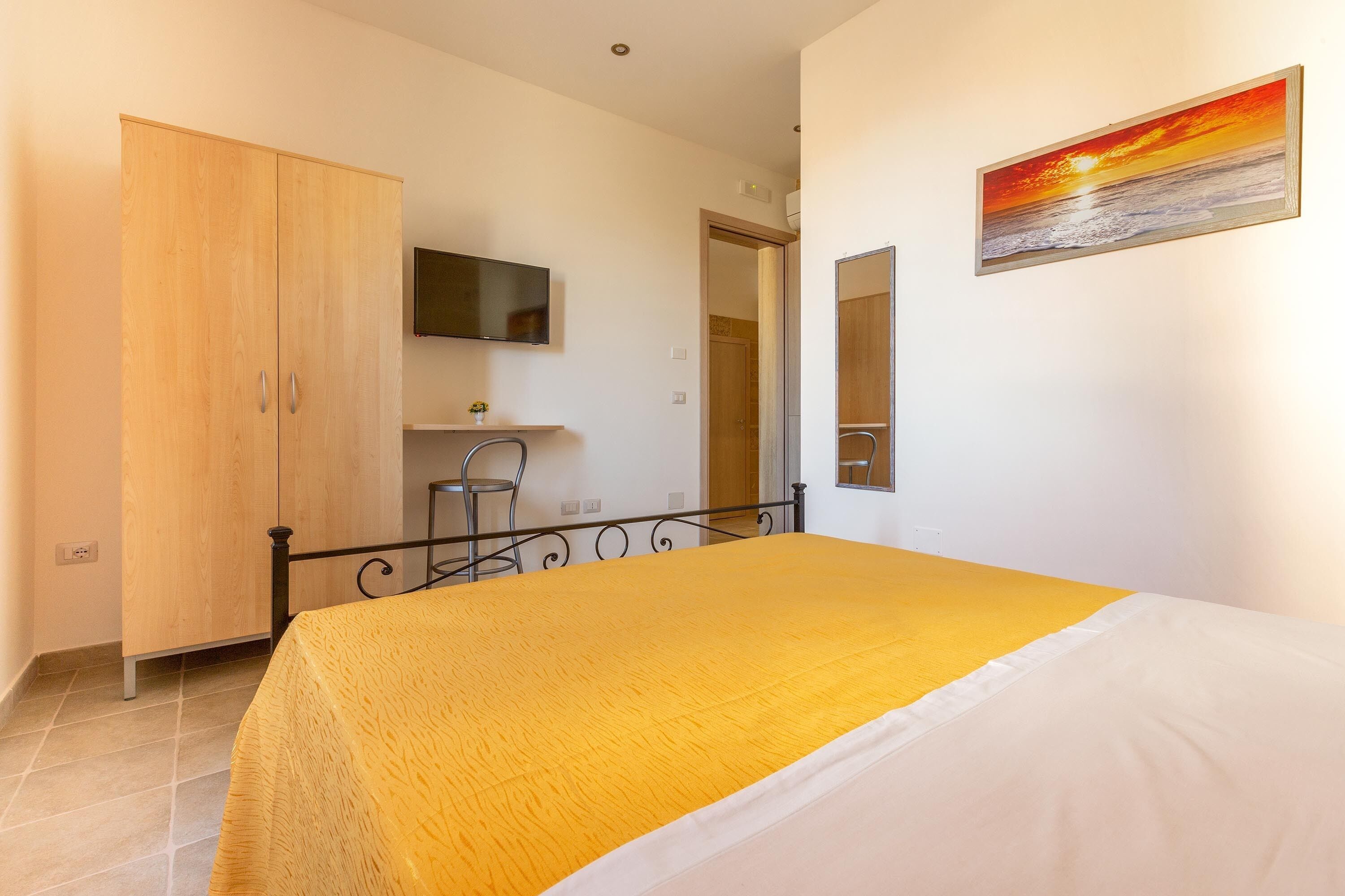 A bedroom with a bed, a wardrobe, a television, and a painting.