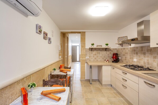 A kitchen with a long countertop, a stove, and a sink. There are cabinets and a ceiling light.