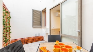 Un pequeño comedor con una mesa dispuesta para cuatro personas, una silla de mimbre y un banco de madera.