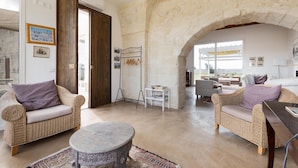 A spacious living area with wicker furniture, a round coffee table, and a stone archway. - 1891 Falcon Home Resort (Lizzanello)