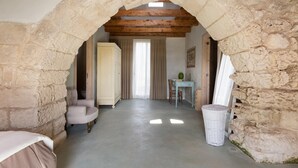 A room with a stone archway, a bed, a chair, a table, and a window with curtains. - 1891 Falcon Home Resort (Lizzanello)