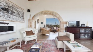 A spacious living area with a large painting, a white sofa, a coffee table with books, and a view through an archway to an outdoor patio. - 1891 Falcon Home Resort (Lizzanello)