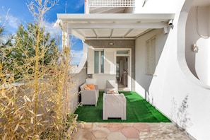 A small patio with a green artificial turf, white wicker furniture, and a view of the interior through a door. - 1807 Villa Iolanda (Porto Cesareo)