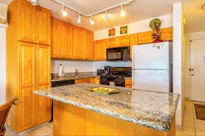 Una cocina con armarios de madera, encimera de granito, microondas, refrigerador y estufa.