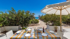 An outdoor dining area with a table set for two, overlooking a beach and a clear blue sky. - 1906 Villa Sara (Porto Cesareo)
