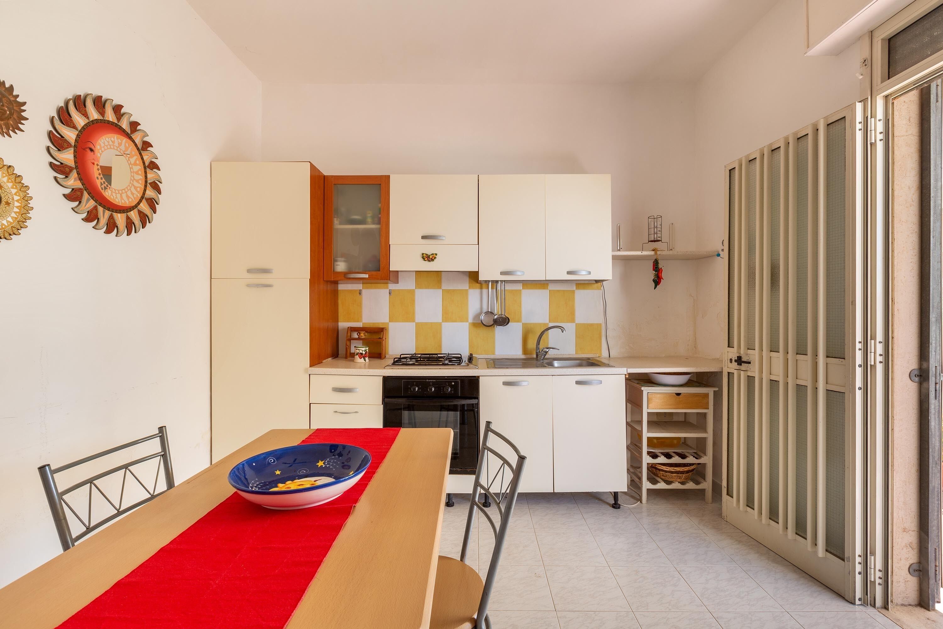 A compact kitchen with white cabinets, a red tablecloth, and a bowl on the table.