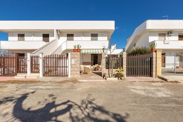 A two-story residential building with a gated entrance, outdoor seating area, and potted plants.