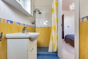 A bathroom with a sink, shower, and a bed in the adjacent room.