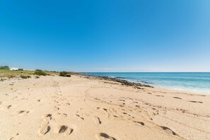 A sandy beach with footprints leading to the water, a rocky shoreline, and a clear blue sky.