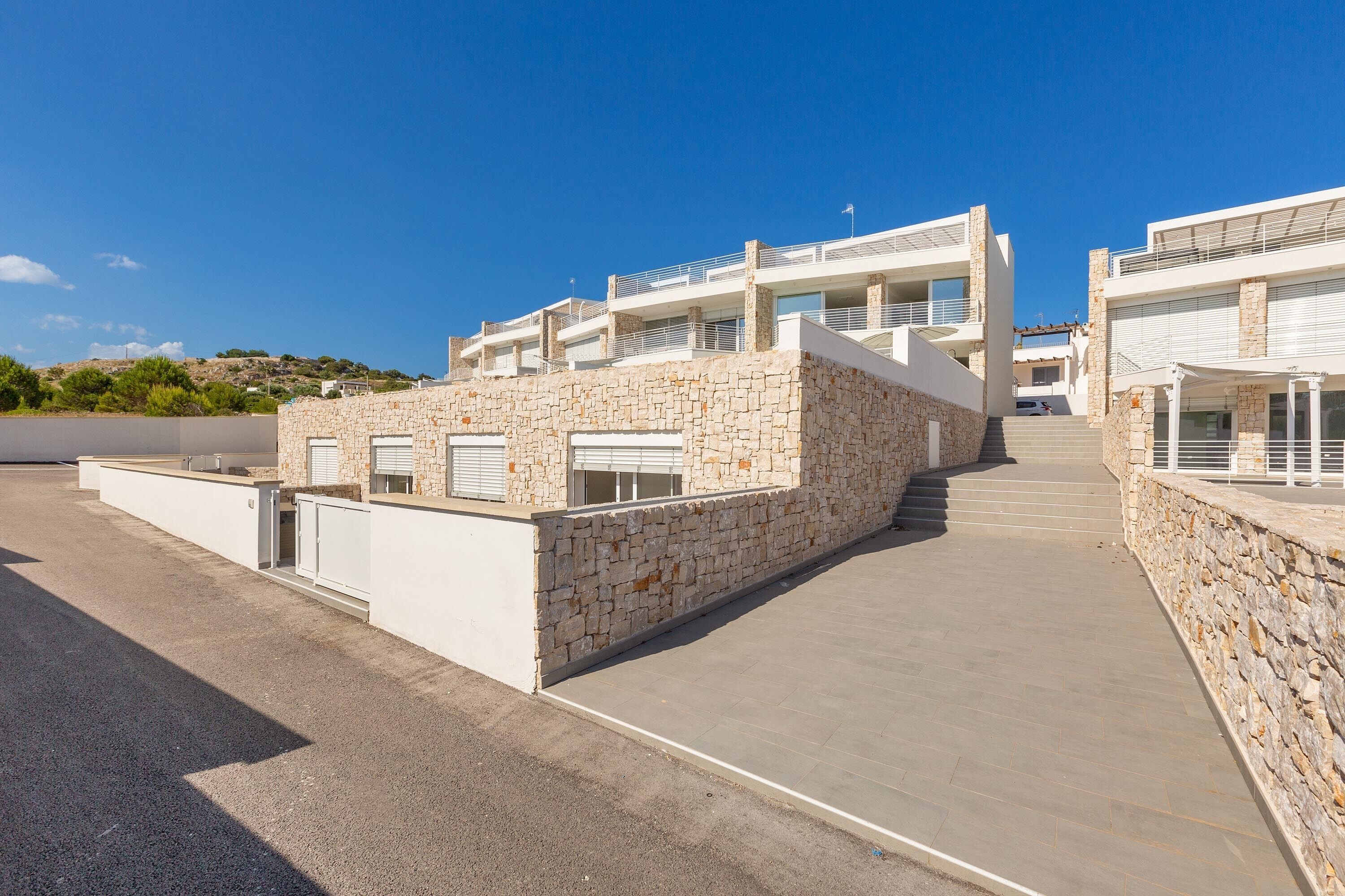 Un bâtiment moderne avec une façade en pierre, de nombreux balcons et un ciel dégagé.