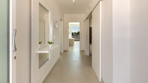 Un pasillo moderno con suelo de tonos claros, paredes blancas y una puerta a la izquierda.
