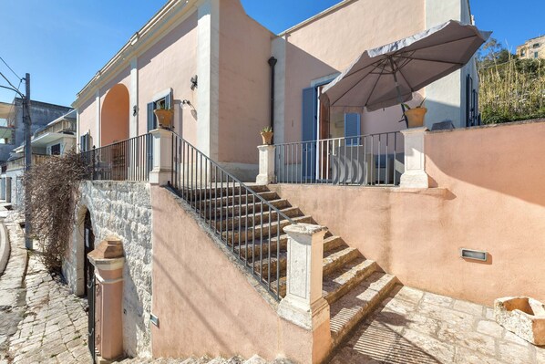 A staircase leading to a building with a balcony, a potted plant, and a metal railing.