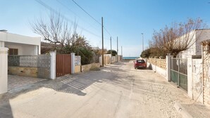 A residential street with houses, a red car parked on the right, and a clear sky. - 1826 Villetta Solaire (Porto Cesareo)