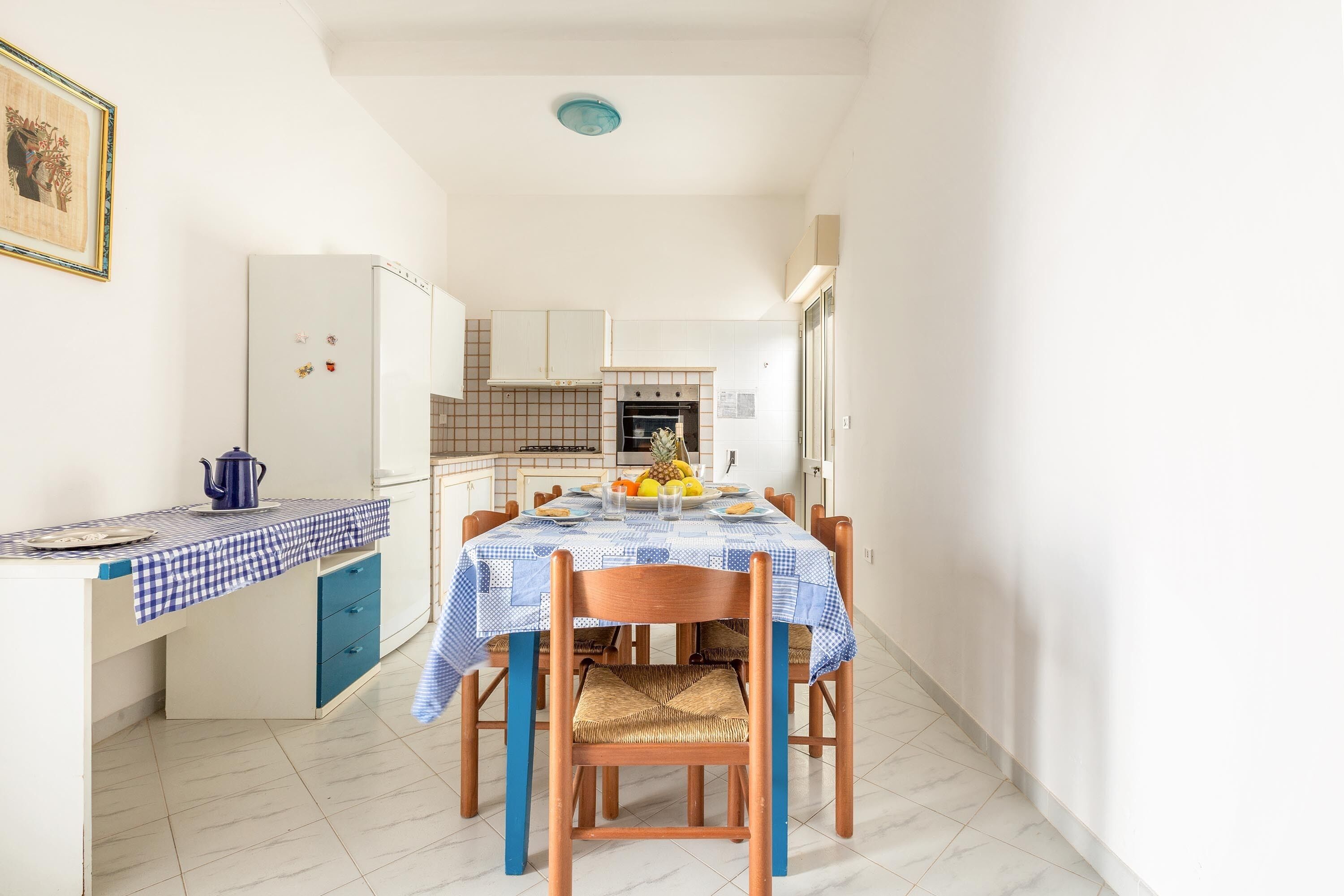 A compact kitchen with a dining area, featuring a checkered tablecloth, wooden chairs, and a tiled floor.