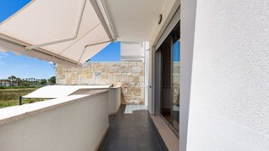 Uma varanda com parede de pedra, toldo branco e porta de vidro que dá para uma área coberta.