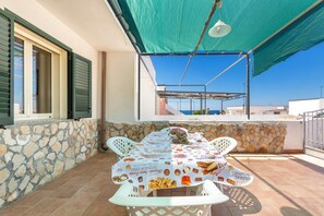 Een buitenmeedeel met een tafel, overdekt met een tafelkleed waarop afbeeldingen van eten staan, omringd door stenen muren en uitzicht op de zee.