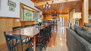 A wooden dining table with chairs, a kitchen area with appliances, and a staircase.