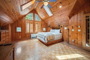 A wooden cabin bedroom with a bed, a ceiling fan, a skylight, and a large window. - Brooklake - Custom built home on Dodge Pond, with 250' on Dodge Pond Stream too (Rangeley)