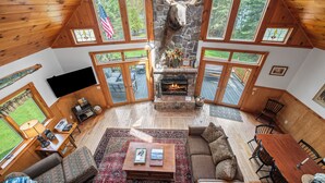 A spacious living area with a stone fireplace, wooden ceiling, and large windows.