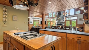 A kitchen with wooden cabinets, a large island with a stove, and a stone fireplace.