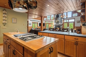 A kitchen with wooden cabinets, a large island with a stove, and a stone fireplace.