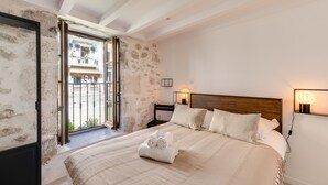 Un dormitorio con una cama grande, cabecera de madera, mesita de noche con lámpara y vistas al balcón exterior.