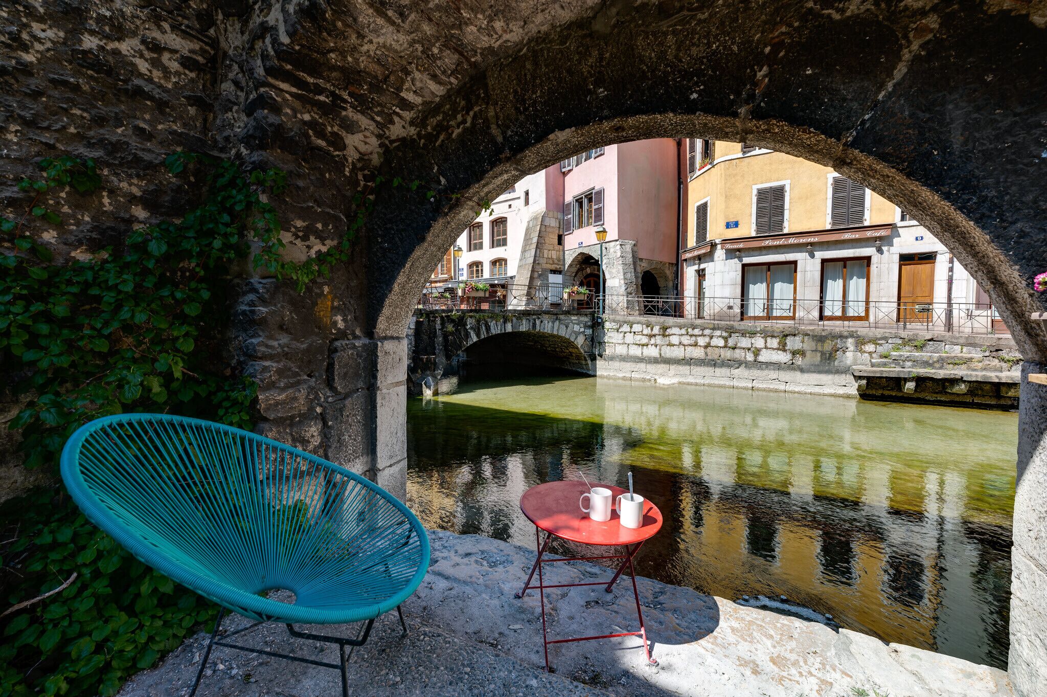 Un puente de piedra sobre un canal con una silla y una mesa junto al agua.