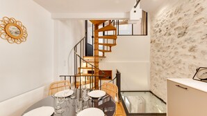 Un comedor moderno con una mesa redonda preparada para cuatro personas, una escalera de caracol y una pared de piedra.