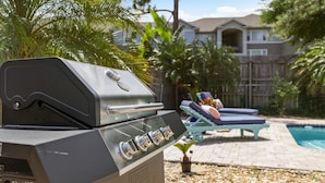 A barbecue grill with four burners, a control panel, and a stainless steel finish. In the background, there is a swimming pool with lounge chairs and a wooden fence. - Comfy Mayo Retreat: Pool & Close to Beach (Jacksonville Beach)