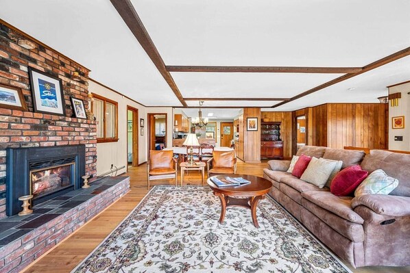 A cozy living room with a fireplace, a wooden ceiling, a sofa with cushions, and a patterned rug. - Spacious Ski Home - 10 Miles to Stowe 3 bed 4 bath (Morristown)