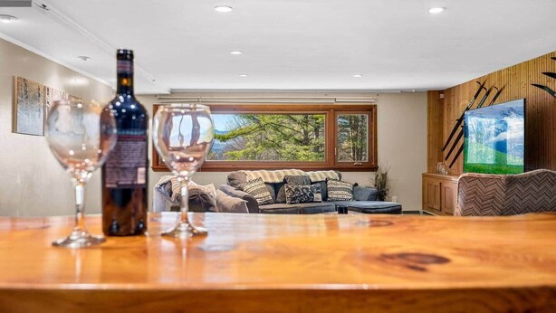 A living room with a wooden table, two wine glasses, a bottle, a sofa, and a TV.
