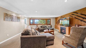 A living room with a sofa, armchair, coffee table, fireplace, TV, and ski equipment.