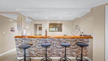 A bar area with a stone wall, three stools, and a wooden counter.