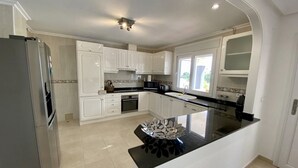 A modern kitchen with white cabinetry, a black countertop island, and a stainless steel refrigerator. -  Luxury Front-Line Golf Villa with Private Pool & Panoramic Views (Orihuela)