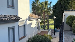 A courtyard with a white building, a palm tree, and a small garden area. -  Luxury Front-Line Golf Villa with Private Pool & Panoramic Views (Orihuela)