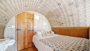 A bedroom with a wooden door, a bed with a patterned bedspread, and a wooden ceiling. - Luxury Pod-sleeps 2-hot Tub-pets-garden (Sheerness)