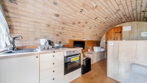 A compact kitchen with a brick wall, wooden ceiling, and a small dining area. - Luxury Pod-sleeps 2-hot Tub-pets-garden (Sheerness)