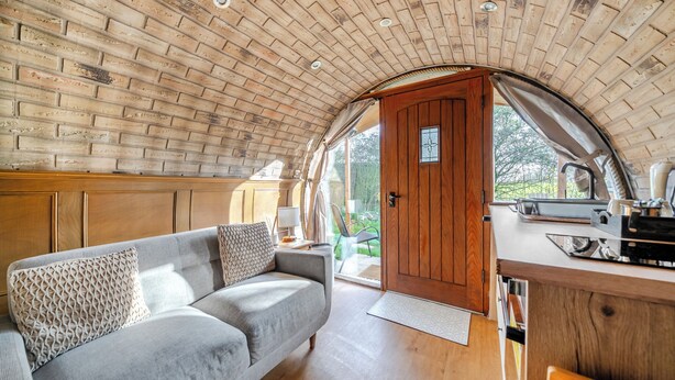 A cozy living area with a sofa, wooden ceiling, and a view through a door. - Luxury Pod-sleeps 2-hot Tub-pets-garden (Sheerness)