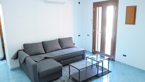 Un salón moderno con un sofá gris, una mesa de centro de vidrio y una puerta que da a un balcón.