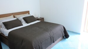 Una cama bien hecha con colcha marrón oscuro y almohadas, un cabecero de madera y una mesita de noche con lámpara y caja de pañuelos.