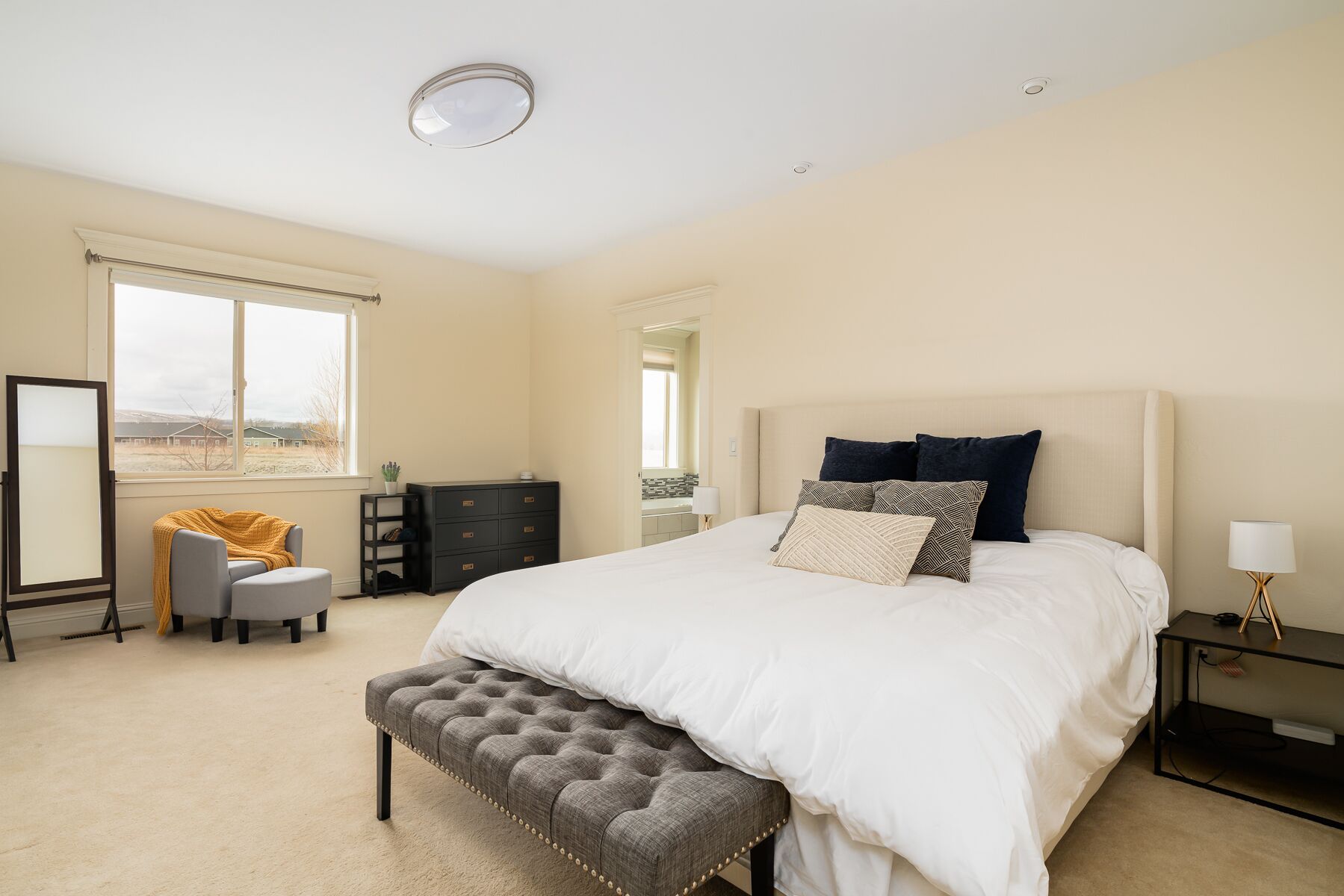 A bedroom with a large bed, a bench, a dresser, a desk, and a mirror.