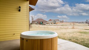 Una bañera de hidromasaje de madera en un patio trasero, con una casa amarilla al fondo.