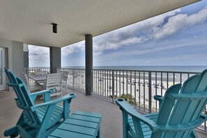 Enjoy the ocean view from this balcony with a beach view, featuring a comfortable seating area with two Adirondack chairs and a bench.