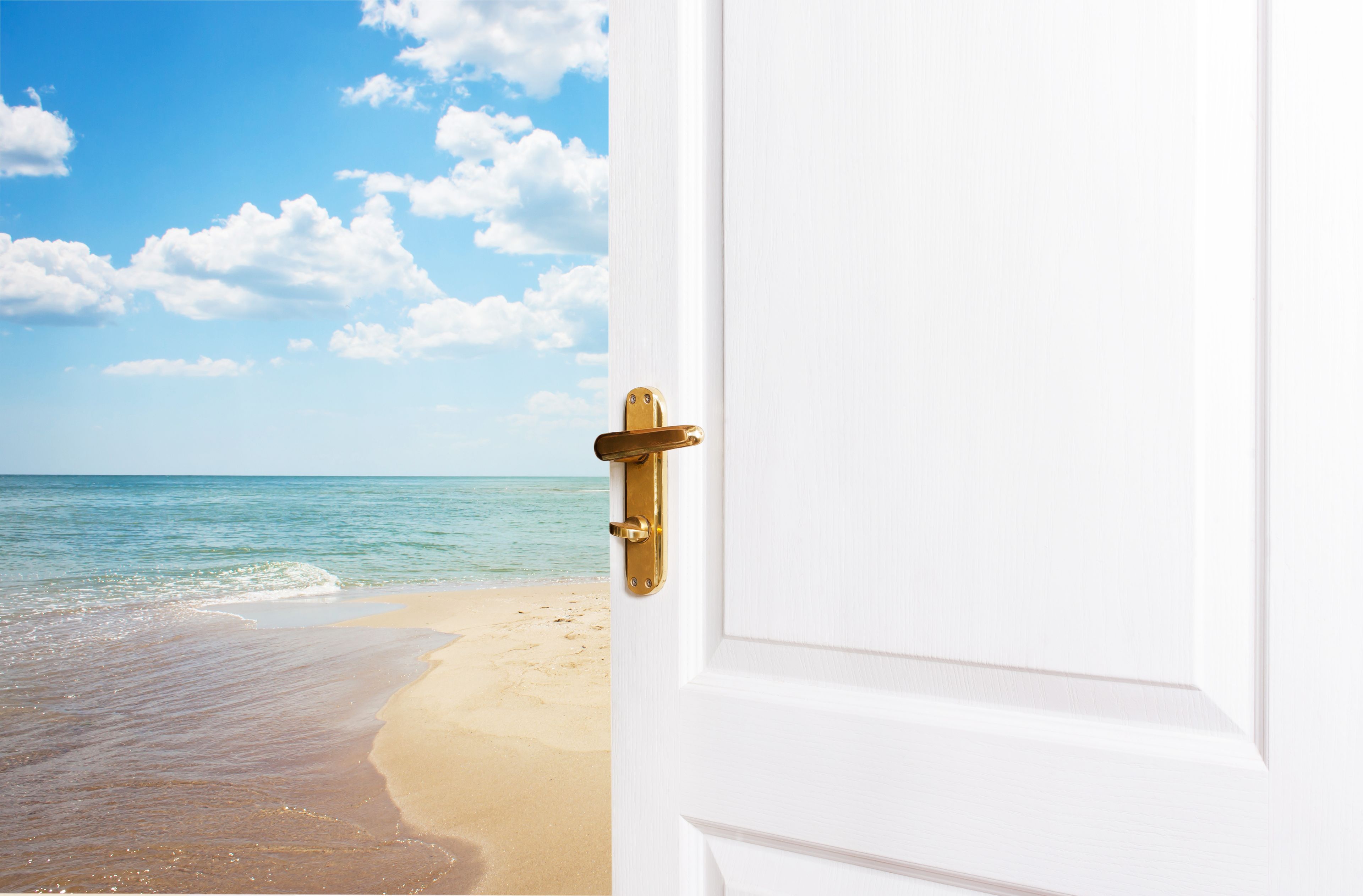 A white door with a brass handle, leading to a beach with clear skies and calm sea.