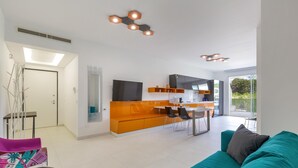 Un espace de vie moderne avec un canapé turquoise, une petite table et un coin cuisine doté de meubles orange.